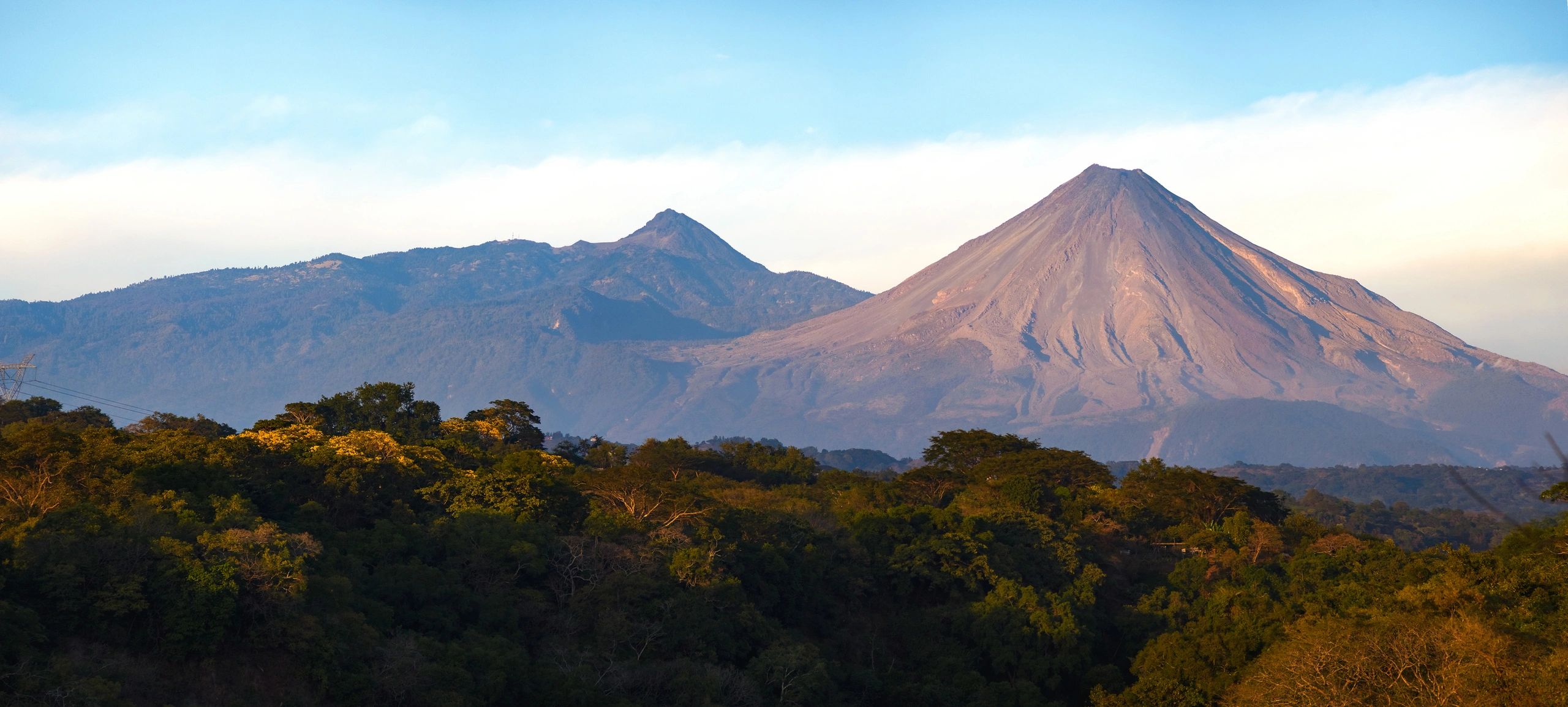 Volcanic eruption plume rising above a mountainous landscape.